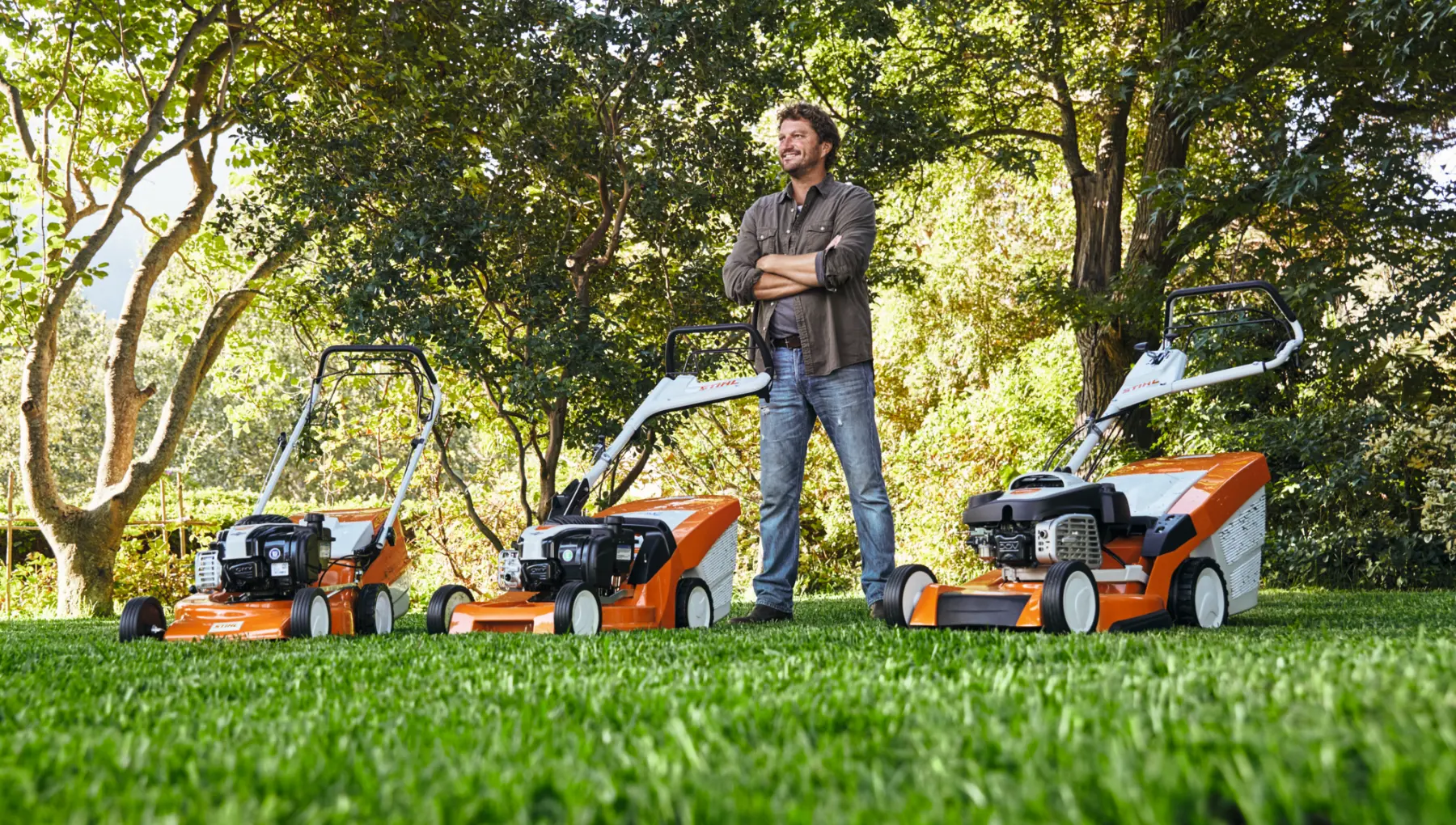 Legjobb fűnyíró kiválasztásához szolgáló kép. Egy férfi áll három STIHL fűnyíró mellett.